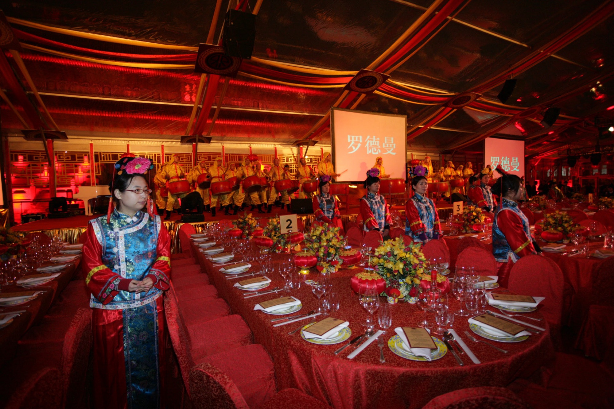 A greeter in palace dress beside long red-draped dinner tables