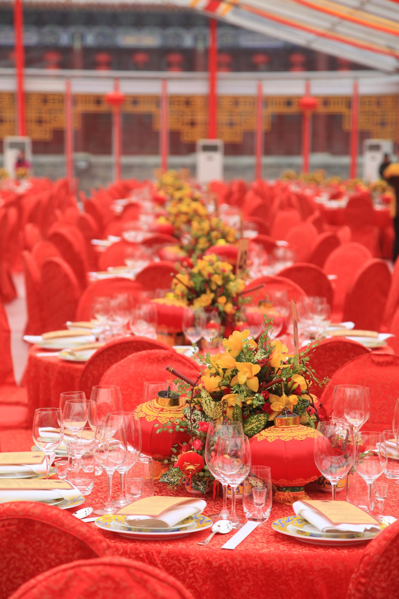 Long dinner tables dressed in red with yellow floral centerpieces