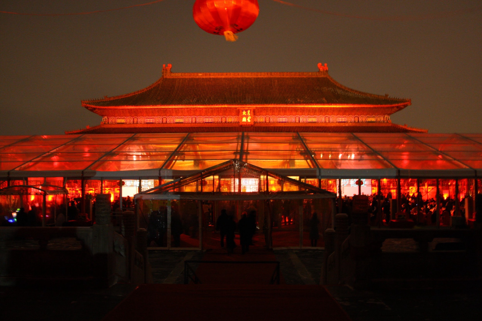 A palace hall glowing red behind the clear dinner tent