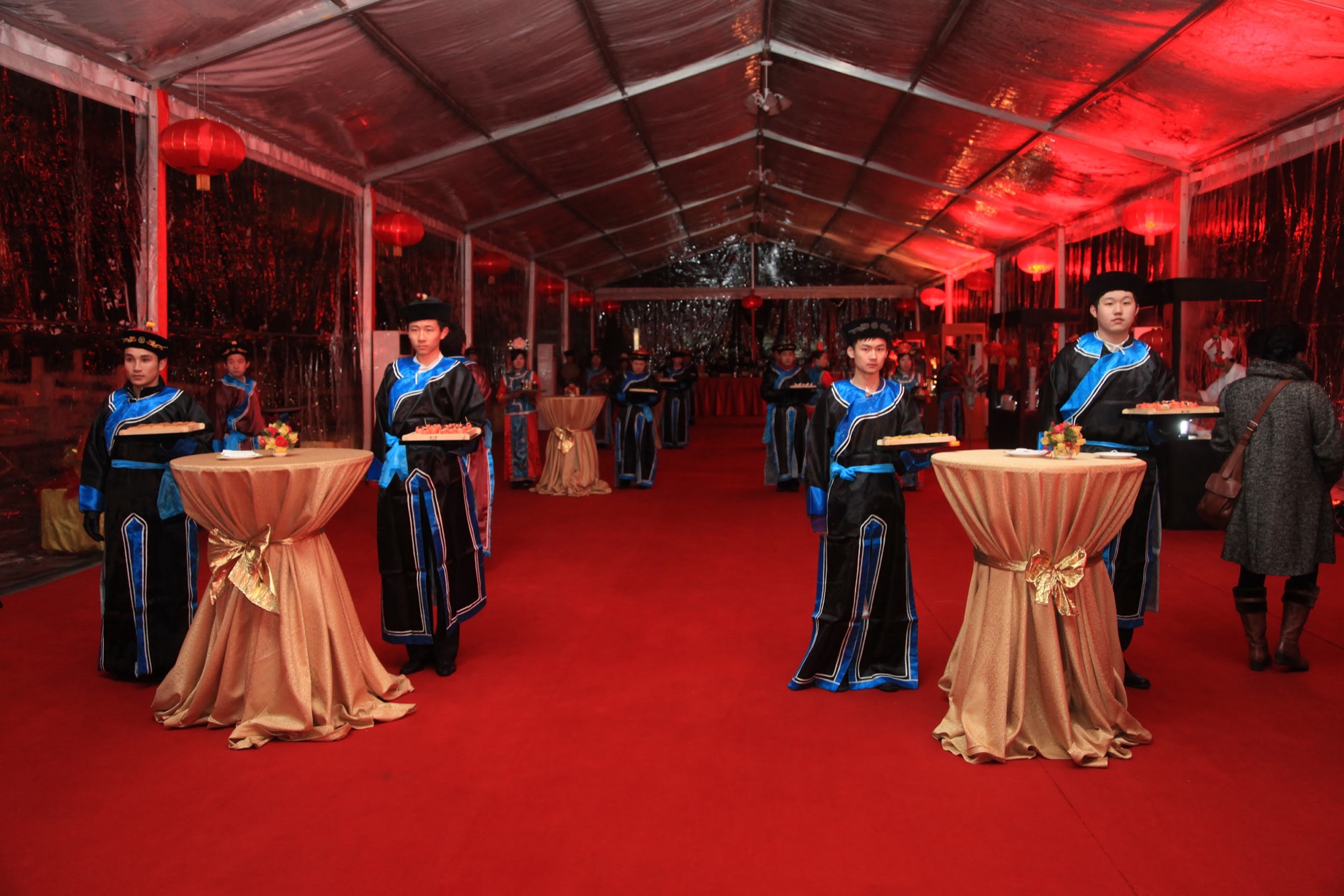 Servers in palace dress at cocktail tables inside the clear tent