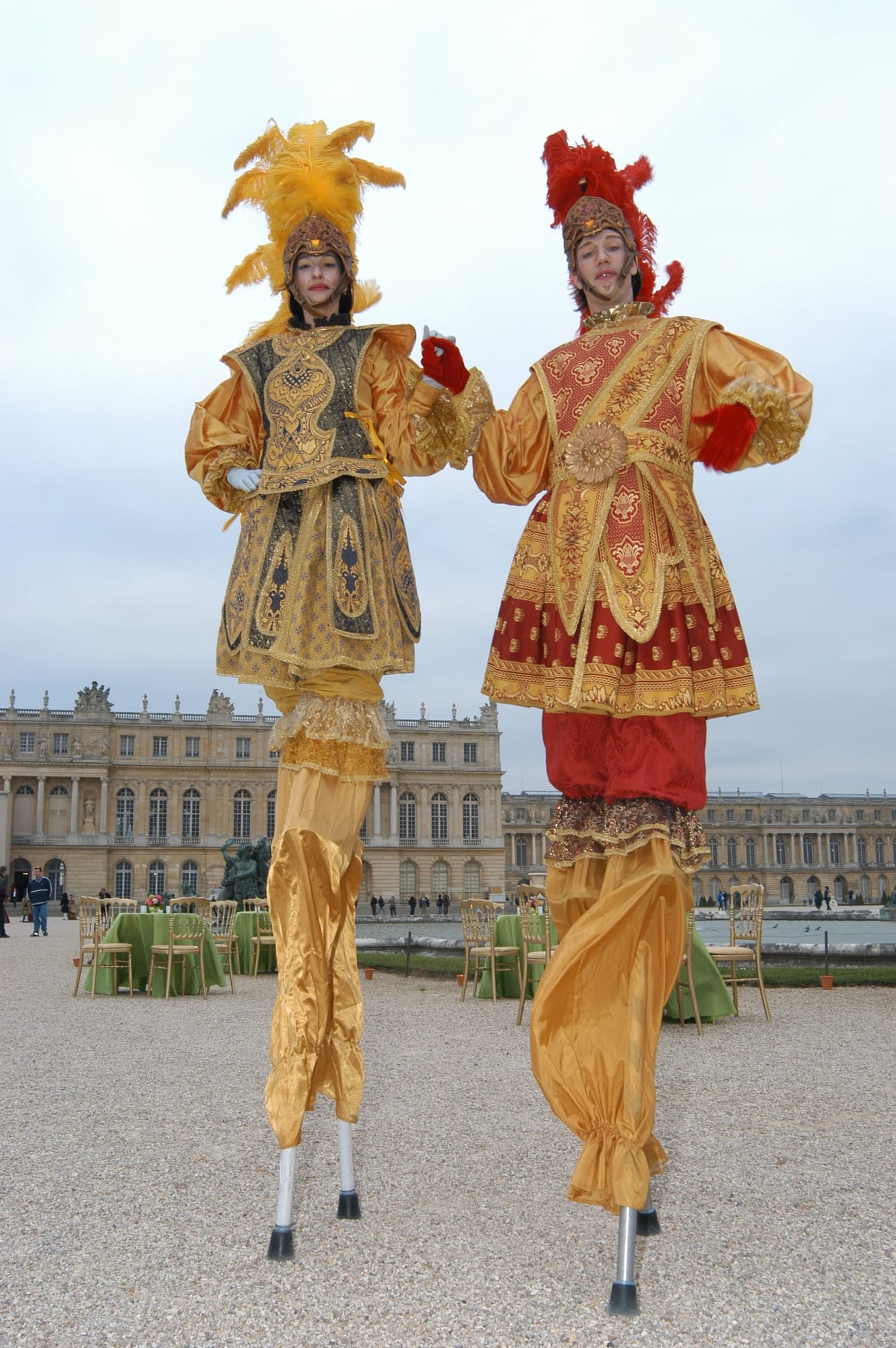 Stilt walkers in gold court costume before the palace